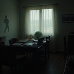 A cluttered and dimly lit remote workspace blending with personal space, illustrating blurred boundaries and hidden warning signs of overwork.